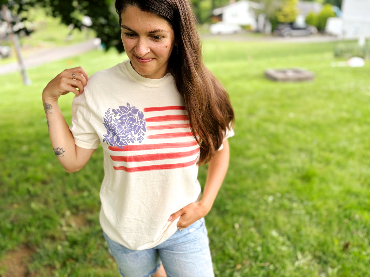 woman with tattoos on arm wearing fourth of july graphic tee featuring blue hand drawn flowers and red stripes