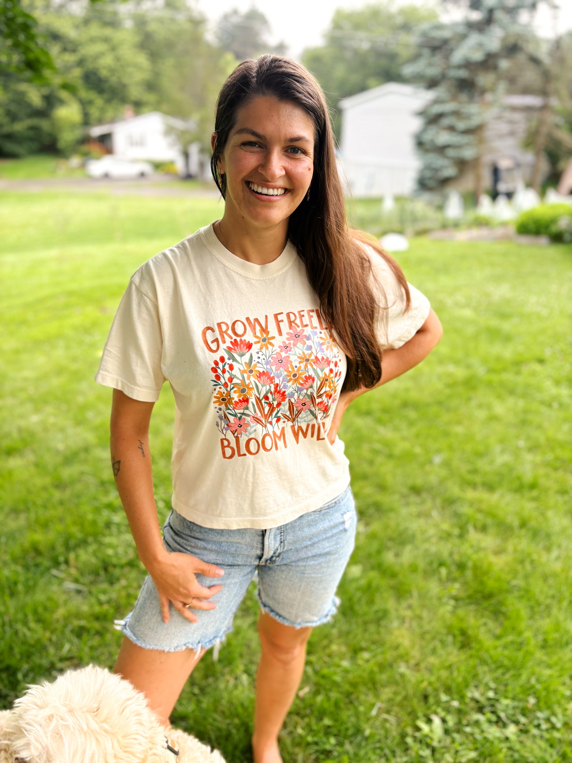 woman with dog in photo wearing cream crop tee with grow freely bloom wildly written on it