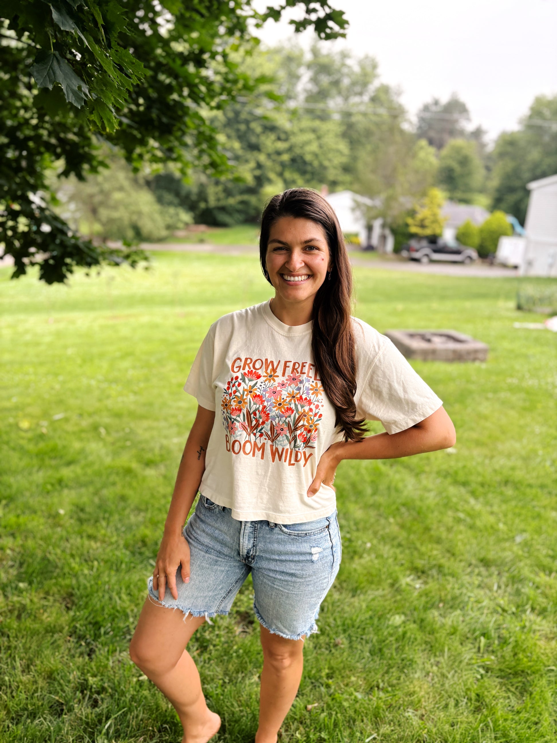 woman smiling at camera while wearing white crop tee with wildflowers 