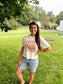 woman smiling at camera while wearing white crop tee with wildflowers 