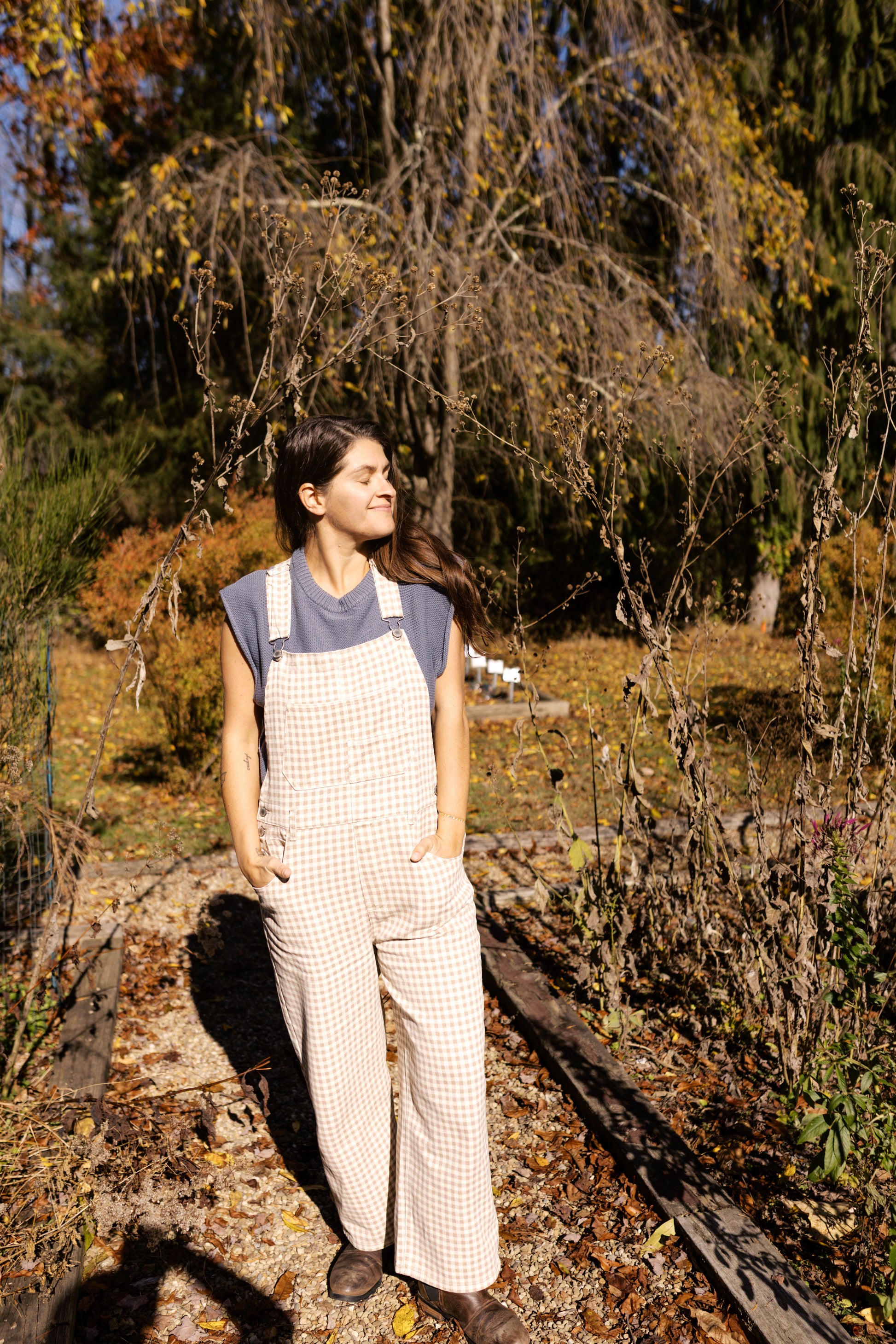 Person wearing checkered overalls standing in a natural setting with trees and grass.