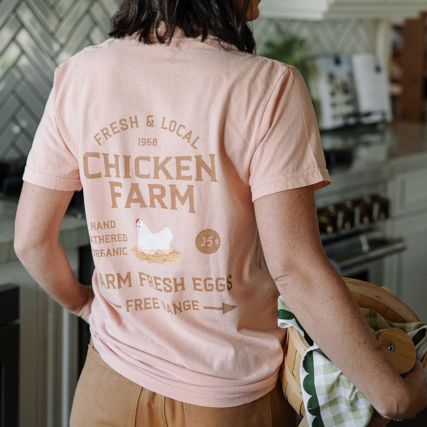 Person wearing a pink t-shirt with 'Chicken Farm' text and graphics in a kitchen.